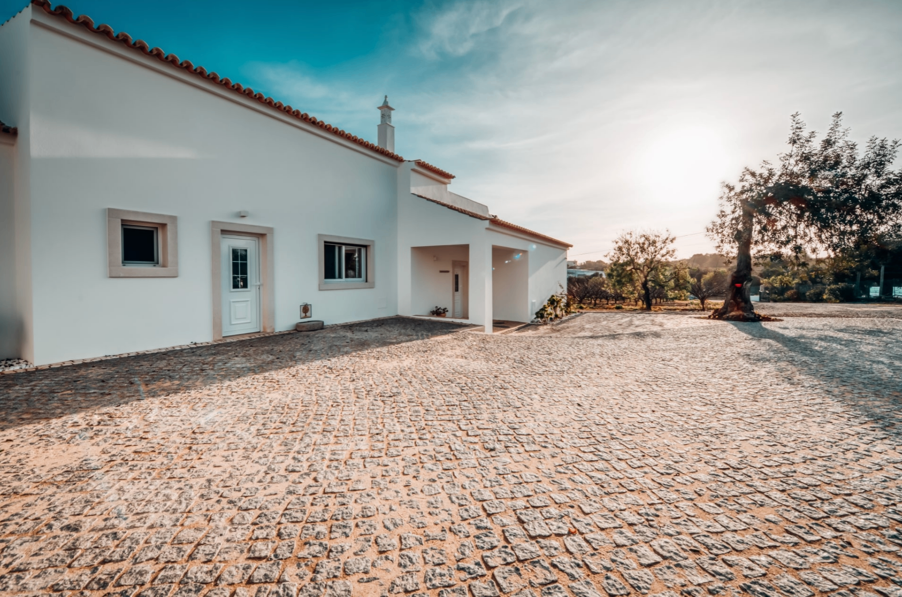 A traditional whitewashed Portuguese villa with terracotta roof tiles and a sunlit cobblestone courtyard